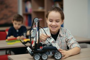 Two boys kids of different age playing with robot toy at school robotics class