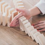 partial view of risk manager blocking domino effect of falling wooden blocks