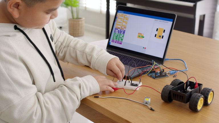 Un joven estudiante asiático aprende a distancia en casa con un coche robot de programación